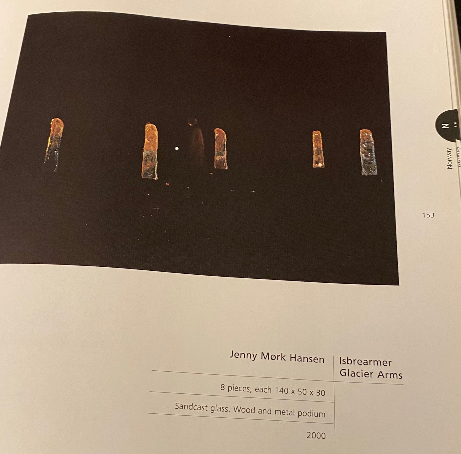Glacier Arms glassart installation by Jenny Mørk featured on a stage surrounded by darkness and a person in a black cape